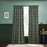 Pair of pencil pleat curtains in the Strawberry Thief design, forest green polyester fabric with bird and strawberry motif, hung on a wooden pole in a green-walled room.