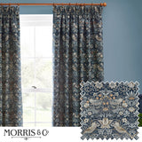 Strawberry Thief pencil pleat curtains in indigo blue, woven jacquard fabric with bird and strawberry motif, shown pleated on a wooden pole beside a window.