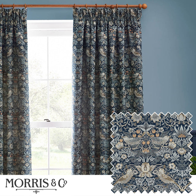 Strawberry Thief pencil pleat curtains in indigo blue, woven jacquard fabric with bird and strawberry motif, shown pleated on a wooden pole beside a window.