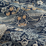 Close-up of Strawberry Thief pencil pleat curtain fabric in indigo, a woven jacquard showing birds, strawberries and trailing floral motifs in orange, grey and cream.
