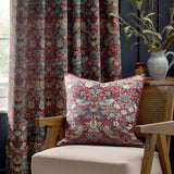 Strawberry Thief Jacquard Velvet Cushion in Berry with bird and floral pattern, styled on a beige armchair against matching curtains in a living room setting.