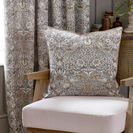 Strawberry Thief Jacquard Velvet Cushion in Biscuit, featuring Morris & Co.'s bird and berry motif, styled on a wooden armchair beside a matching curtain.