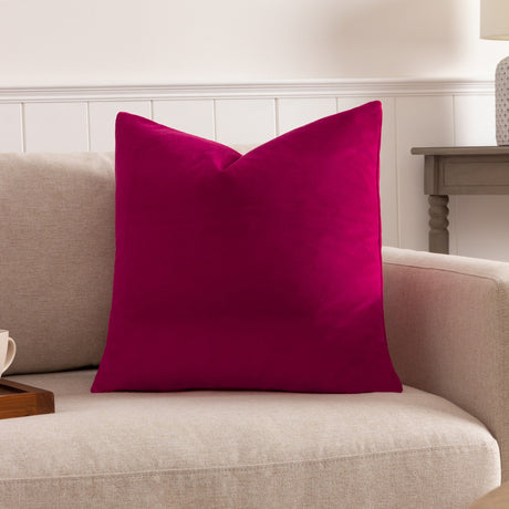 Sunningdale Plain Velvet Cushion in cerise pink, a square scatter cushion with a dense velvet pile, shown on a beige sofa in a living room setting.
