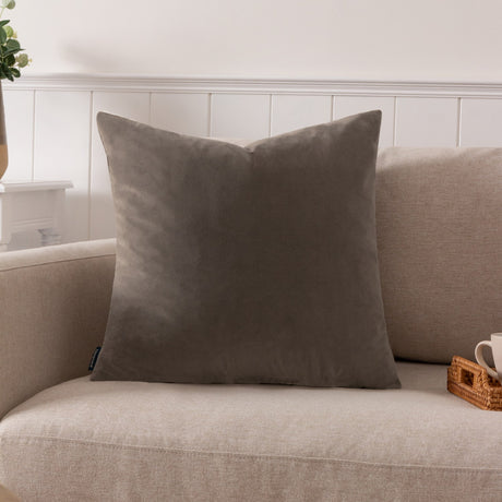 Sunningdale plain velvet cushion in mink, a warm grey-brown square 50 x 50cm design shown on a beige sofa in a living room setting.