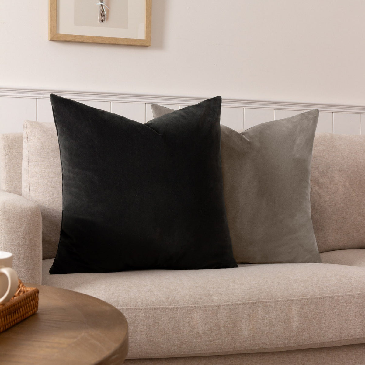 Sunningdale Plain Velvet Cushion in mink, a square 50 x 50cm design shown with a black velvet cushion on a neutral sofa in a living room setting.