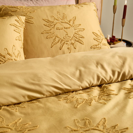 Gold polyester duvet cover set with tufted sun motifs on the duvet and pillowcases, shown on a bed in a bedroom setting.