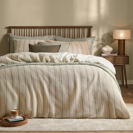 Selby Waffle Cotton Striped Duvet Cover Set in Bay Green/Natural on a bed with matching pillowcases and cushions, in a bedroom with wooden headboard and bedside lamp.