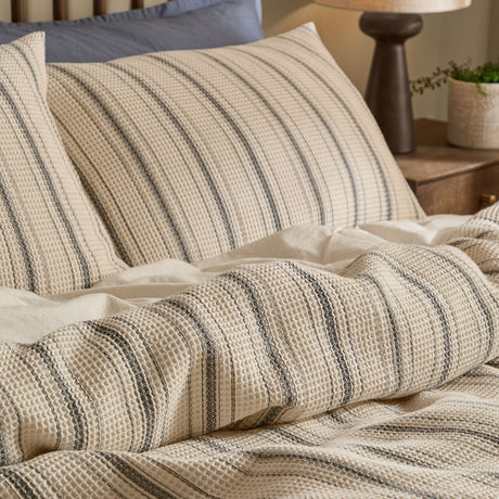 Selby waffle cotton duvet cover set with coal stripes on a natural ground, shown on a bed with matching pillowcases and a plain white sheet beneath.