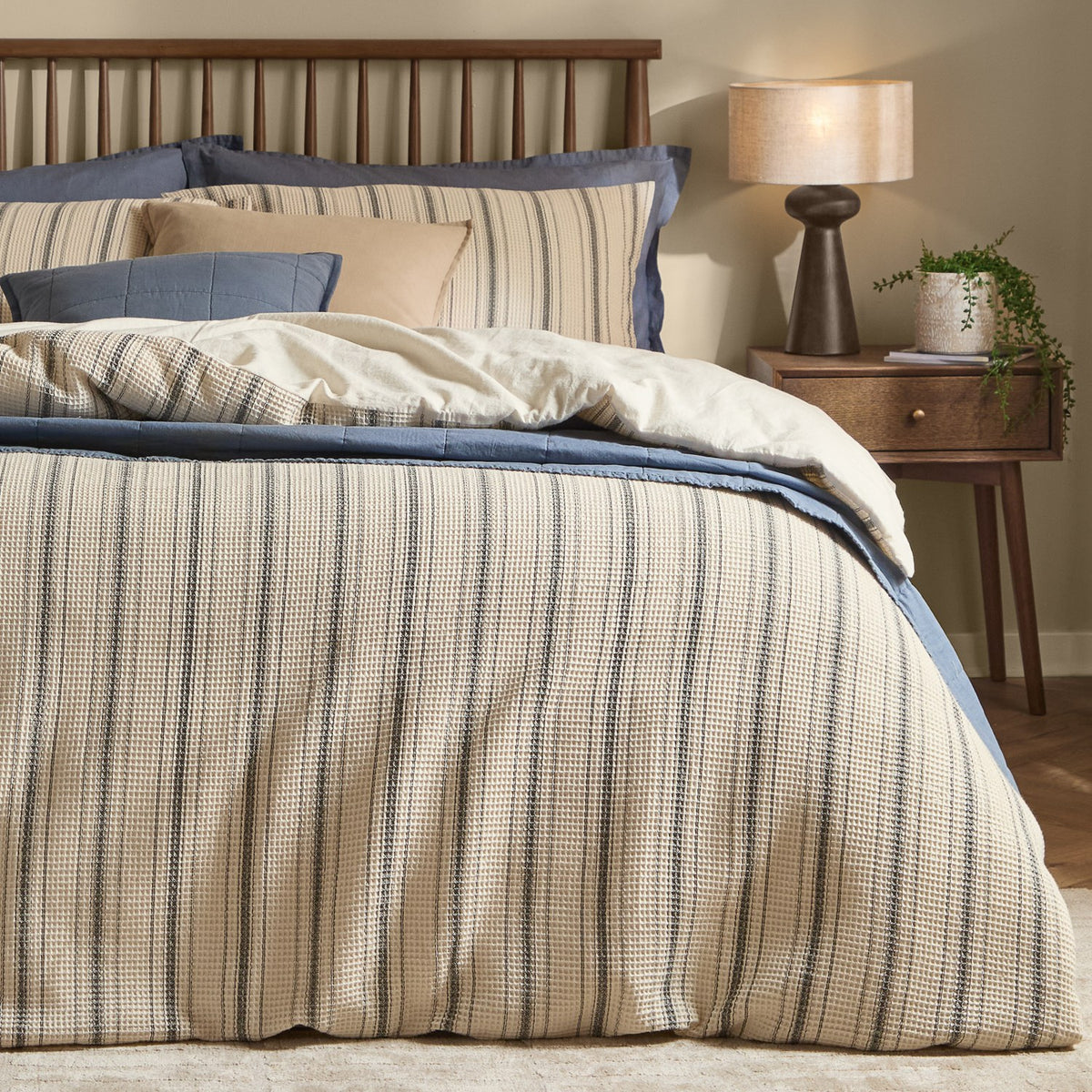 Selby Waffle Cotton Striped Duvet Cover Set in coal and natural, shown on a bed with matching pillowcases, layered blue and cream bedding, wooden headboard and bedside table with lamp.