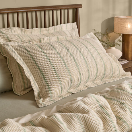 Selby Waffle Percale Cotton Pillowcase Pair in Bay Green/Natural, shown on bed pillows with a matching waffle-weave throw, wooden headboard and bedside lamp in a bedroom setting.