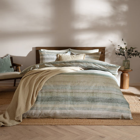Swift Cotton Striped Duvet Cover Set in Eucalyptus, dressed on a bed with matching pillowcases and cushions, showing a soft green, sage and sand toned stripe in a modern bedroom setting.