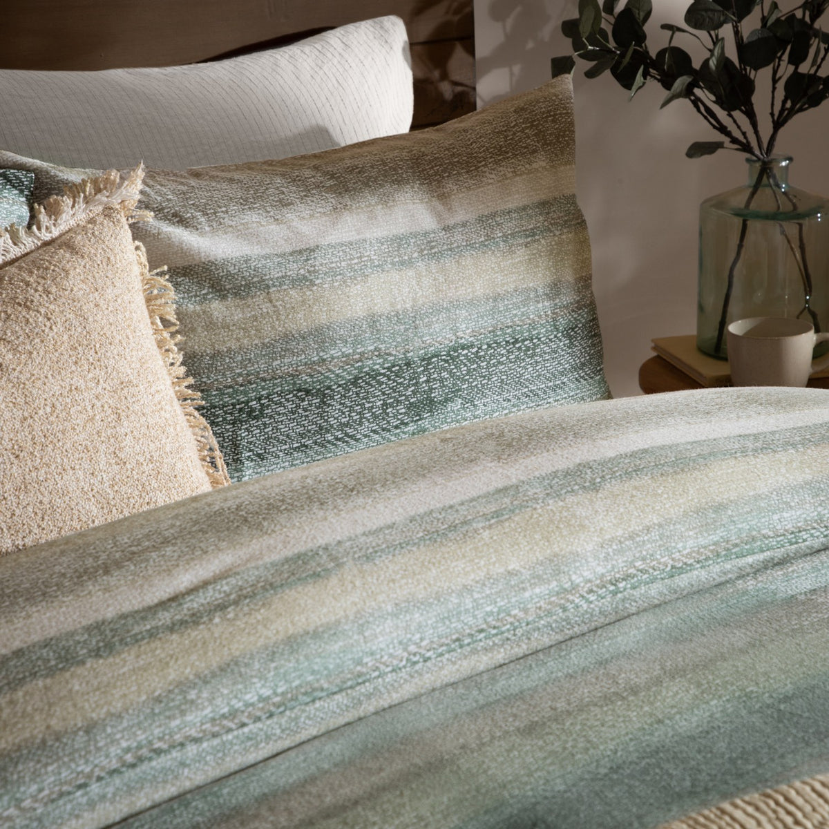 Swift Cotton Striped Duvet Cover Set in Eucalyptus, showing a blurred green, sage and sand striped cotton duvet with matching pillows on a bedroom bed.