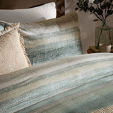 Swift Cotton Striped Duvet Cover Set in Eucalyptus, showing a blurred green, sage and sand striped cotton duvet with matching pillows on a bedroom bed.