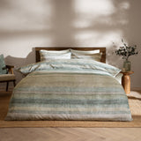 Swift Cotton Striped Duvet Cover Set in Eucalyptus, styled on a bed with matching pillowcases in muted green, sage and sand stripes, set in a bedroom with wooden headboard and side table.
