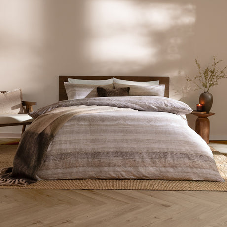 Swift Cotton Striped Duvet Cover Set in natural tones, styled on a bed with pillows and a throw in a warm-toned bedroom setting.