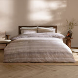 Swift Cotton Striped Duvet Cover Set in Natural, dressed on a bed with matching pillowcases, showing a soft blurred stripe pattern in muted beige and cream tones in a bedroom setting.
