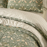 Strawberry Thief quilted cotton bedspread in forest green, showing bird and berry pattern face, striped percale reverse, and matching pillowcase in a bedroom setting.