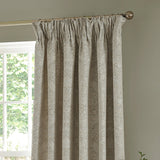 Strawberry Thief Jacquard Linen pencil pleat curtains in beige, shown hanging from a pole with pinch-pleat header, woven floral and bird pattern, in a room beside a window.