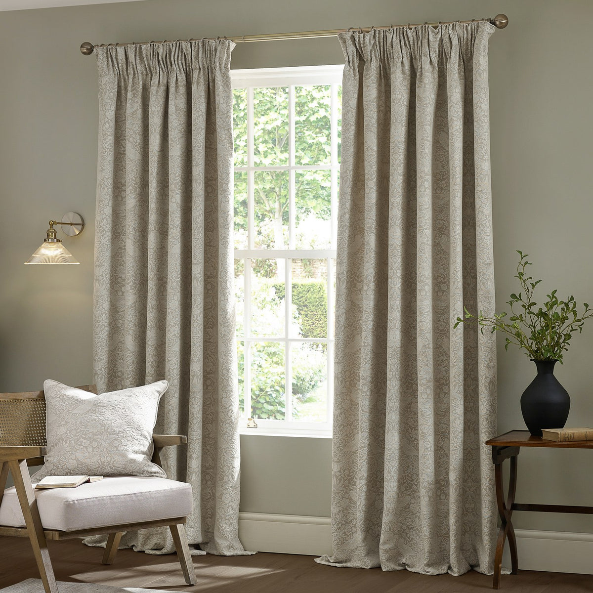 Strawberry Thief jacquard linen pencil pleat curtains in beige, floor-length with tonal woven pattern, shown either side of a window in a living room setting.