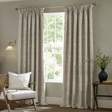 Strawberry Thief jacquard linen pencil pleat curtains in beige, floor-length with tonal woven pattern, shown either side of a window in a living room setting.