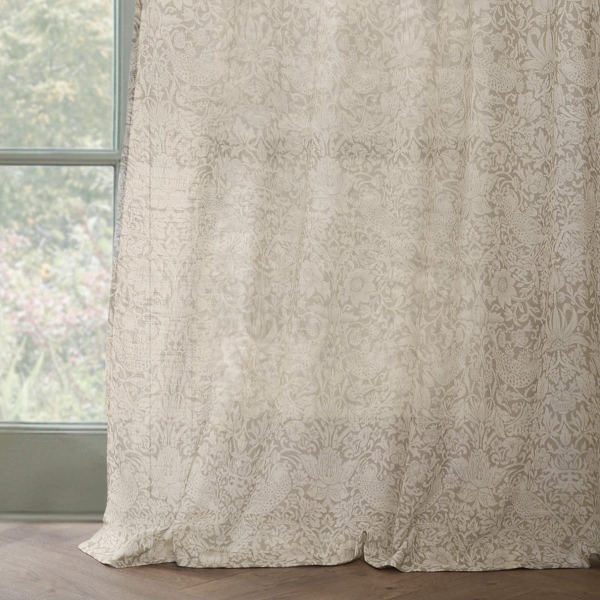 Strawberry Thief Floral Linen Curtain Panel in cream, hanging beside a window with a tonal bird and floral pattern on semi-sheer voile fabric.