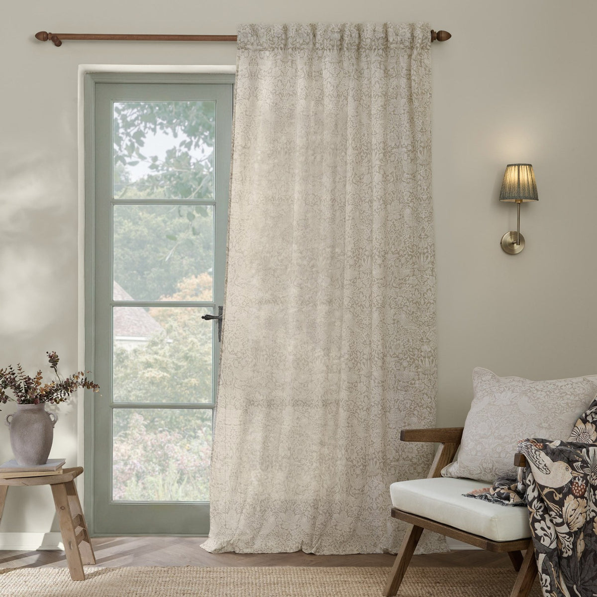 Strawberry Thief Floral Linen Curtain Panel in cream and natural tones, hung on a wooden rod beside a glazed door in a living room setting.