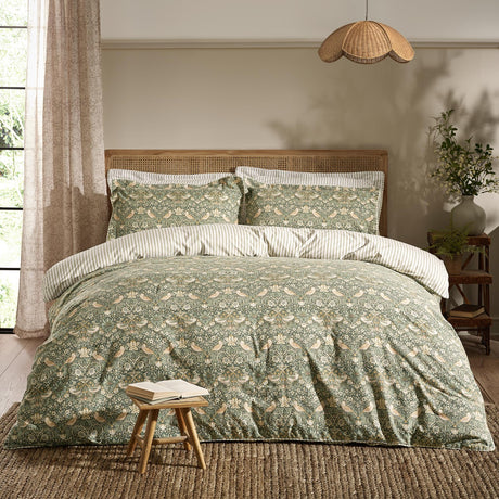 Strawberry Thief Cotton Floral Duvet Cover Set in forest green with bird and berry print, styled on a bed with striped reverse pillowcases in a rustic bedroom setting.