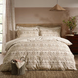 Bedroom scene with a Strawberry Thief cotton floral duvet cover set in natural beige tones, styled with striped reverse pillowcases on a rattan headboard bed.
