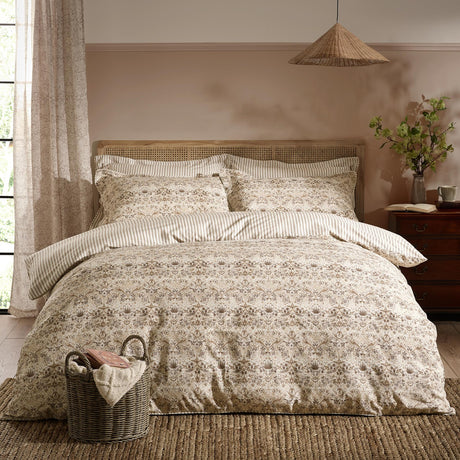 Bedroom scene with a Strawberry Thief cotton floral duvet cover set in natural beige tones, styled with striped reverse pillowcases on a rattan headboard bed.