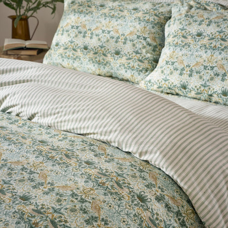 Strawberry Thief cotton duvet cover set in sage green, showing bird-and-floral print pillowcases paired with matching green ticking-stripe reverse on a bed.