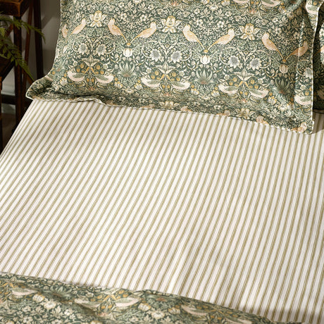 Fitted sheet in green and cream striped cotton percale, styled on a bed with Strawberry Thief patterned pillowcases in forest green.