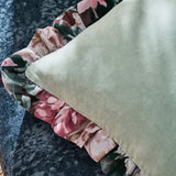 Close-up of the Tahiti Velvet Cotton Cushion in Duck Egg, showing the plain green cotton velvet face edged with a pink and green floral print frill, set on a dark textured fabric surface.