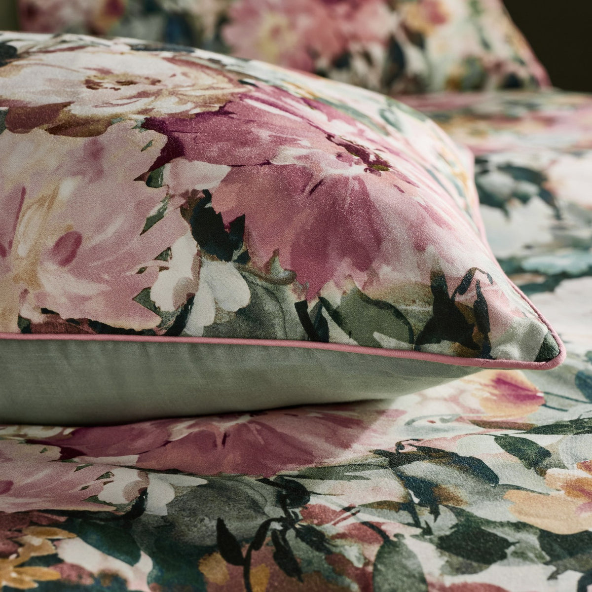 Tahiti Cotton Floral Duvet Cover Set in Spring, close-up of pink piped pillowcase with watercolour floral print and green foliage, plain green reverse, matching duvet cover on bed.