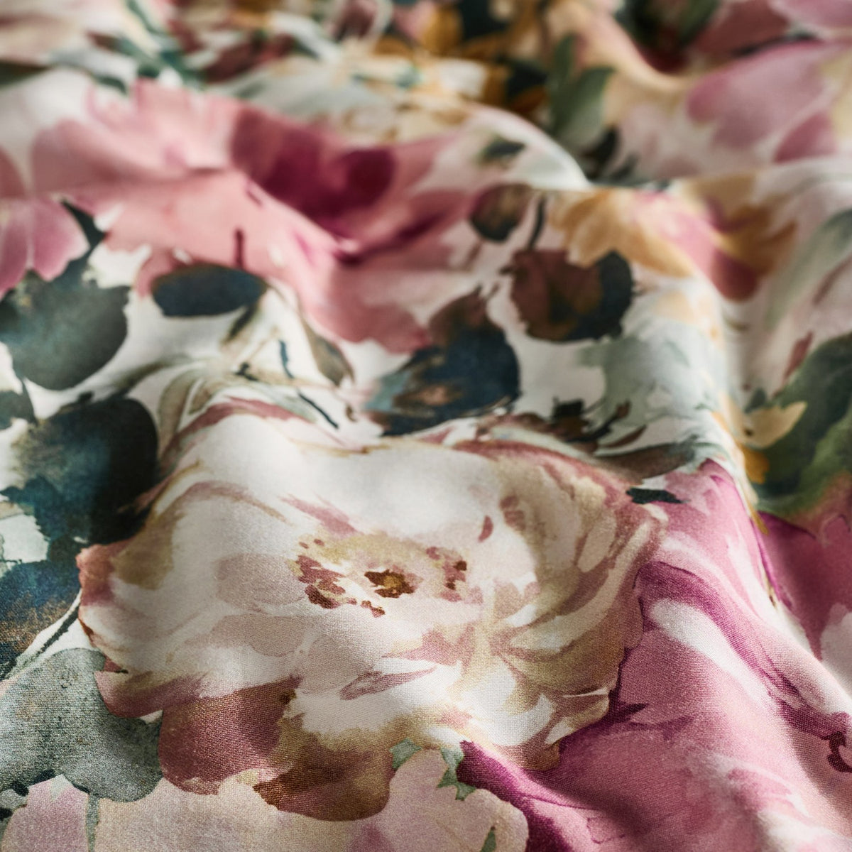 Tahiti Cotton Floral Duvet Cover Set in Spring, close-up of cotton sateen fabric with watercolour blooms in dusky pink, cream and amber against deep green foliage.