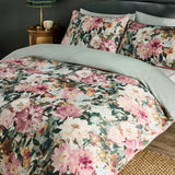 Tahiti Cotton Floral Duvet Cover Set in Spring, shown on a bed with matching pillowcases featuring pink and cream watercolour blooms on green foliage, reverse in plain sage green, bedroom setting.