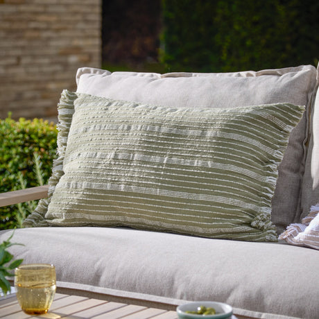 Tide Striped Cotton Cushion in moss green with fringed edges and textured stripe design, styled on a beige outdoor sofa in a garden setting.