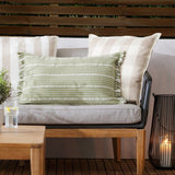 Tide Striped Cotton Cushion in moss green, a rectangular lumbar cushion with fringed edge trim, shown on an outdoor sofa alongside beige check and stripe scatter cushions.