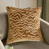 Tierra Abstract Velvet Cushion in brass gold, square with a wandering cut-velvet chevron pattern, shown on a grey armchair.