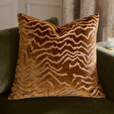 Tierra Abstract Velvet Cushion in bronze, a square cut-velvet cushion with a marbled zigzag pattern, shown on a green sofa in a living room setting.