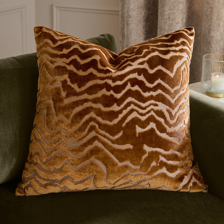 Tierra Abstract Velvet Cushion in bronze, a square cut-velvet cushion with a marbled zigzag pattern, shown on a green sofa in a living room setting.