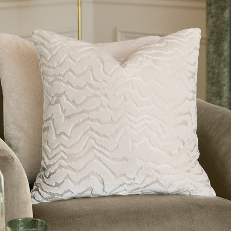 Tierra Abstract Velvet Cushion in white with a raised cut-velvet chevron pattern, shown on a beige armchair in a living room setting.