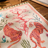Tiger Dream Jungle Polyester Rug in Multi, cream ground with two orange tigers flanking a coral-pink tree, moon and stars motifs, green-striped border, shown on a wooden floor.
