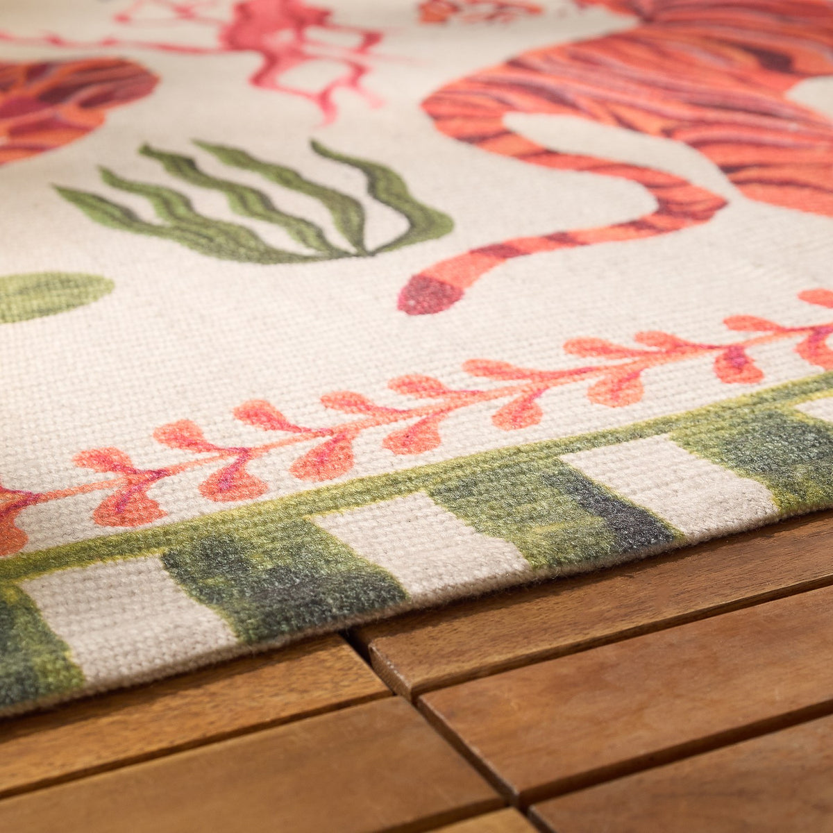 Close-up of the Tiger Dream Jungle Polyester Rug in multi, showing tiger, seaweed motifs and green-and-cream striped border, edge draped over a wooden surface.