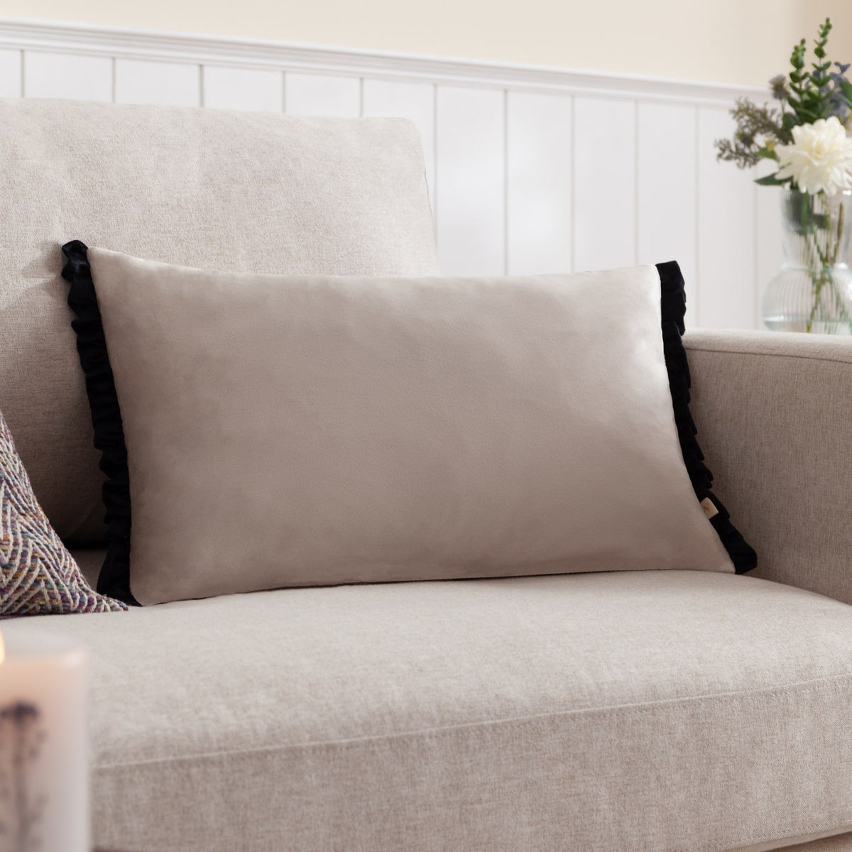 Tilly Plain Velvet Cushion in lace-cream with black frill edges, rectangular bolster shape on a beige sofa in a living room setting.