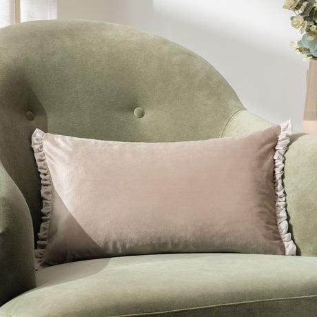 Tilly rectangular velvet cushion in Oyster beige with pale ruffled trim on both short ends, shown on a green velvet armchair.