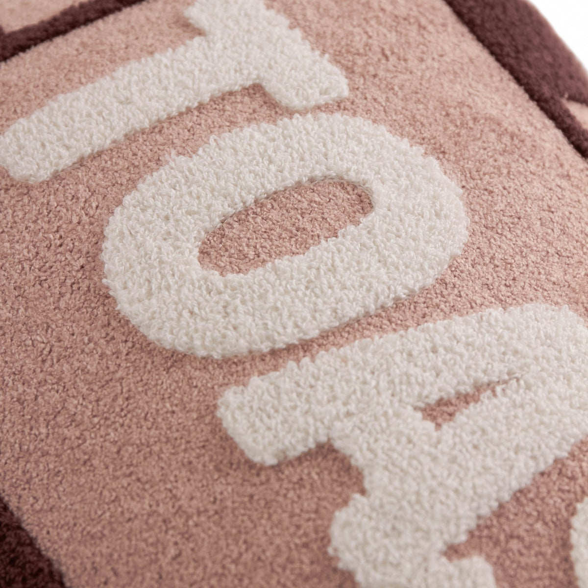 Close-up of the Toasty Striped Velvet Cushion in pink and chocolate, showing cream boucle-textured "Toasty" lettering against a striped fabric surface.