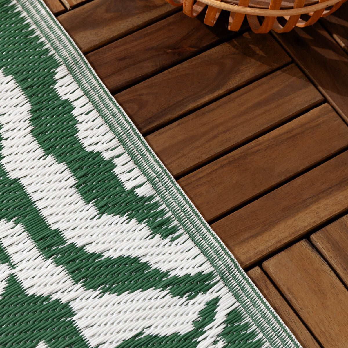 Close-up of the Tocorico Jacquard Jungle Rug in green and white, showing the woven leaf pattern edge against outdoor wooden deck tiles.