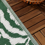 Close-up of the Tocorico Jacquard Jungle Rug in green and white, showing the woven leaf pattern edge against outdoor wooden deck tiles.