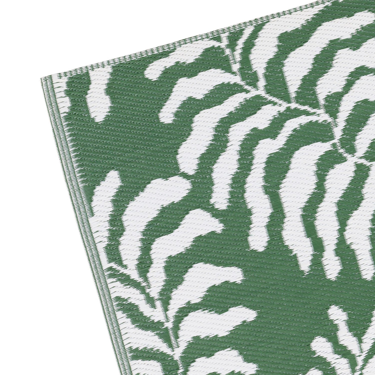 Close-up corner view of the Tocorico Jacquard Jungle Rug in green, showing a bold leaf pattern in green and white woven polypropylene with a finished edge, on a plain white background.