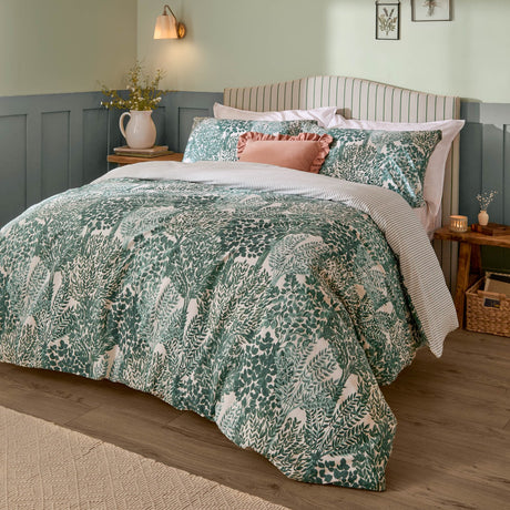 Topiary Reversible Botanical Duvet Cover Set in green on a bed, dense leafy tree print duvet with striped pillowcases, in a bedroom with striped headboard and green wainscoting.